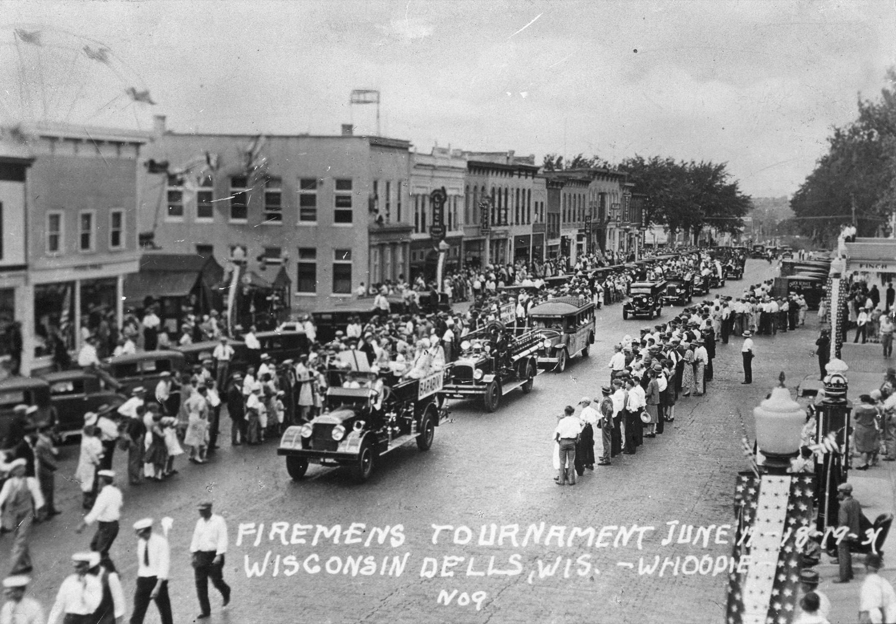 Historic fire apparatus and spectators gathered along a downtown street for a firefighters tournament.